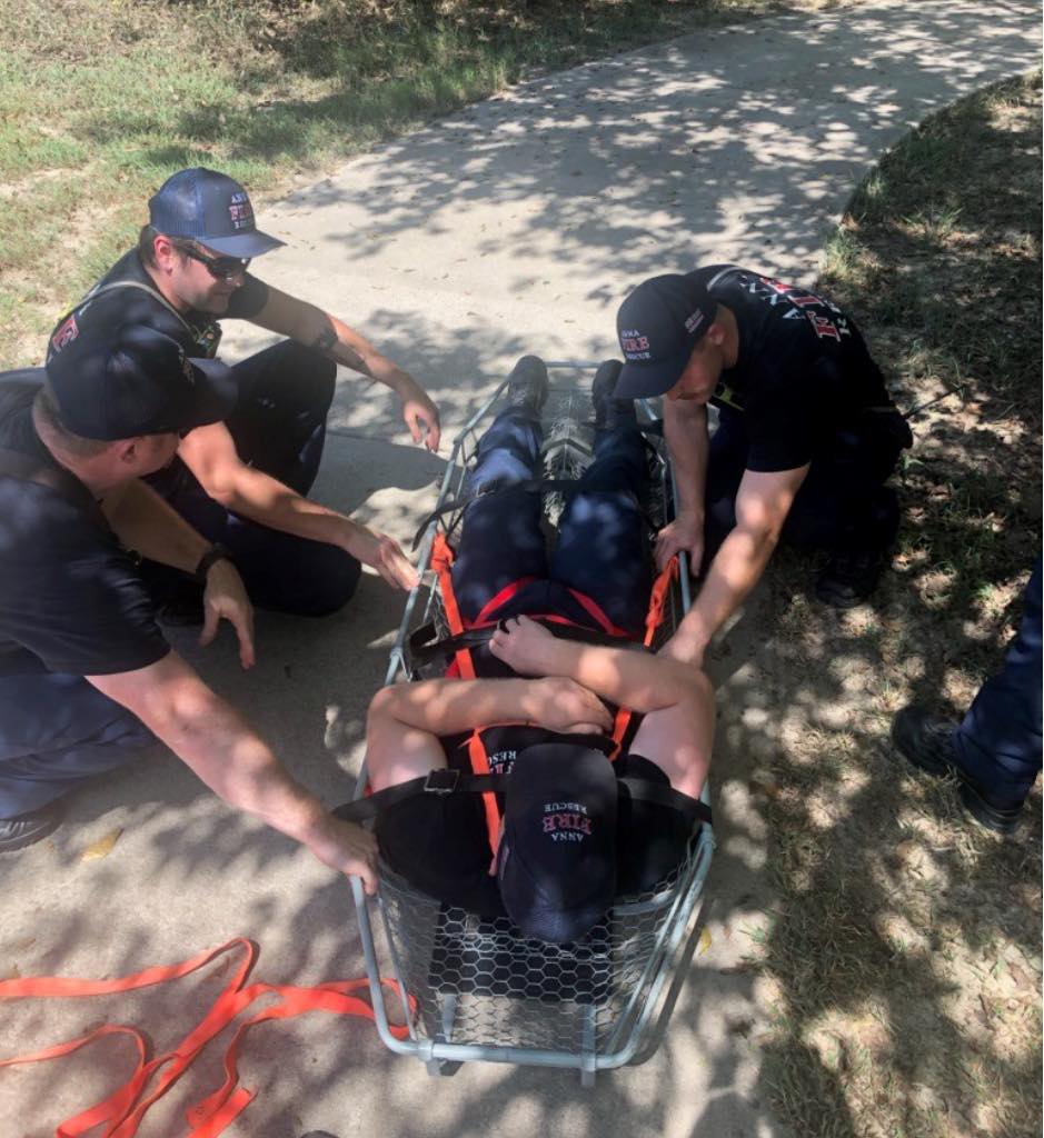 Firefighters crouching around another firefighter laying on a stretcher for training